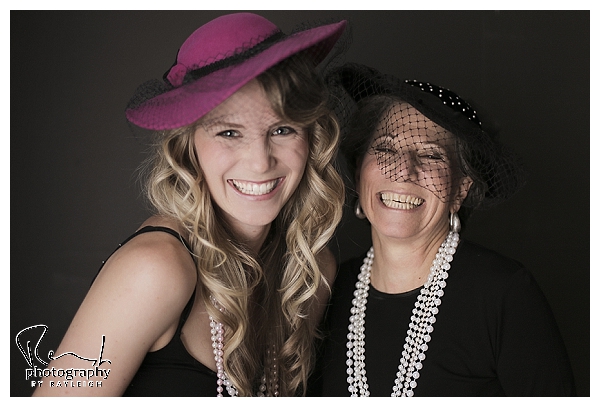 Mother-Daughter session. This image is of an older woman and her grown daughter wearing vintage hats in front of a black background. Photo booth style. Photography by Rayleigh. For more info, visit byrayleigh.com