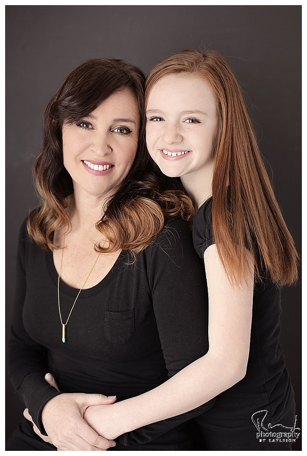 Mother's day portraits with Photography by Rayleigh. This family photo is of a mother and daughter sitting in front of a black background in the studio. For more info, visit byrayleigh.com