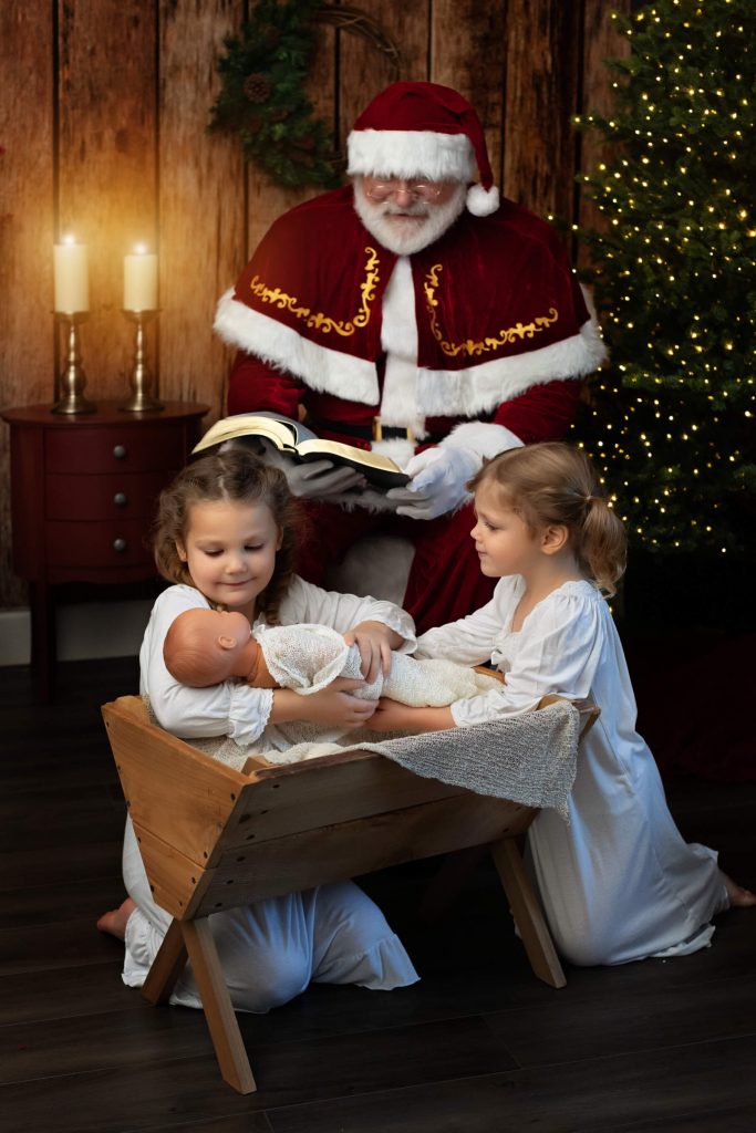 Santa Sessions in Portland, Oregon. Experience the magic of Christmas. Santa is reading the Bible while the children recreate a nativity scene with a manger and baby doll for this photo shoot.