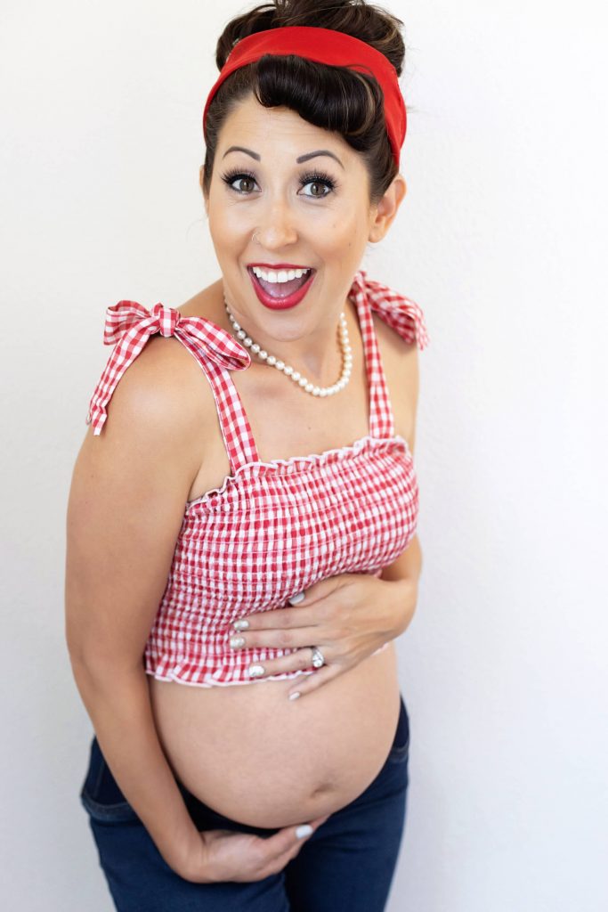50's Style Maternity Photography - Portland Pin Up Photographer. This is a retro inspired maternity portrait taken in a studio in Tualatin, OR. The pregnant woman is holding her belly with a wide eyed smile.