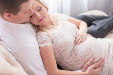 a studio couples maternity photo taken in Portland, OR. This is a lying down pose on a chase.