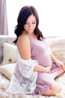 a studio boudoir maternity photo taken in Portland, OR. This is a sitting pose on the bed.
