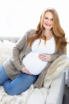 a backlit studio maternity photo taken in Portland, OR. This is a sitting pose on the bed in front of the window.