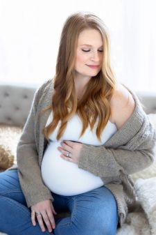 a backlit studio maternity photo taken in Portland, OR. This is a sitting pose on the bed in front of a window.