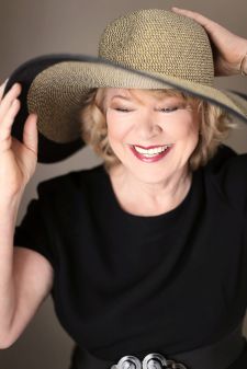 A beauty photo shoot in a studio in Portland, OR. This is a standing pose with a hat against a brown backdrop.