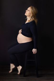 a studio boudoir maternity photo taken in Portland, OR. This is a sitting pose with a black backdrop.