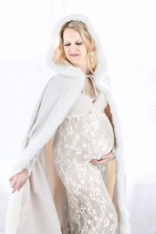 a studio boudoir maternity photo taken in Portland, OR in the winter. This is a standing pose and she is wearing a cape in front of a window.