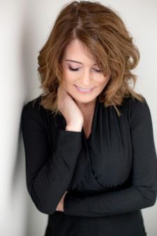 A beauty photo shoot in a studio in Portland, OR. This is a standing wall pose. She is looking down.