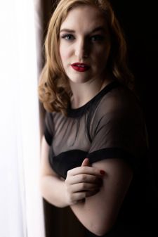 A studio pin-up photo shoot in Portland, OR. This is a dark and moody feel next to a window with a black background.