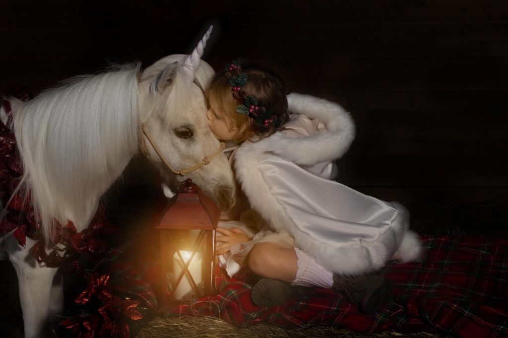 Unicorn Christmas mini sessions near Portland, OR. Stylized fine art portraits that are dark and moody with light effects. This girl is wearing a white winter cloak and holding a glowing lantern.