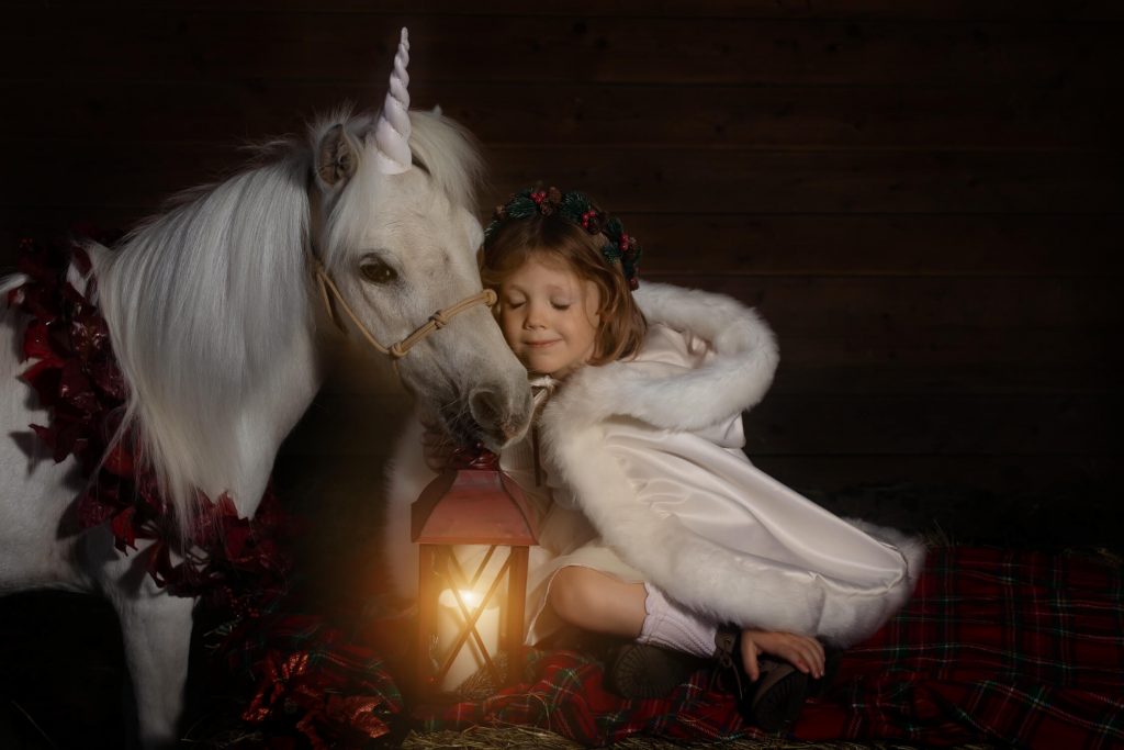 Unicorn Christmas mini sessions near Portland, OR. Stylized fine art portraits that are dark and moody with light effects. This girl is wearing a white winter cloak and holding a glowing lantern.