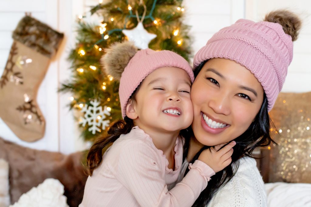 A Christmas Mother-Daughter Session - Portland Family Photographer. An Asian Mom and her young daughter in front of a Christmas tree, wearing winter hats. For more info, visit byRayleigh.com. Photography by Rayleigh