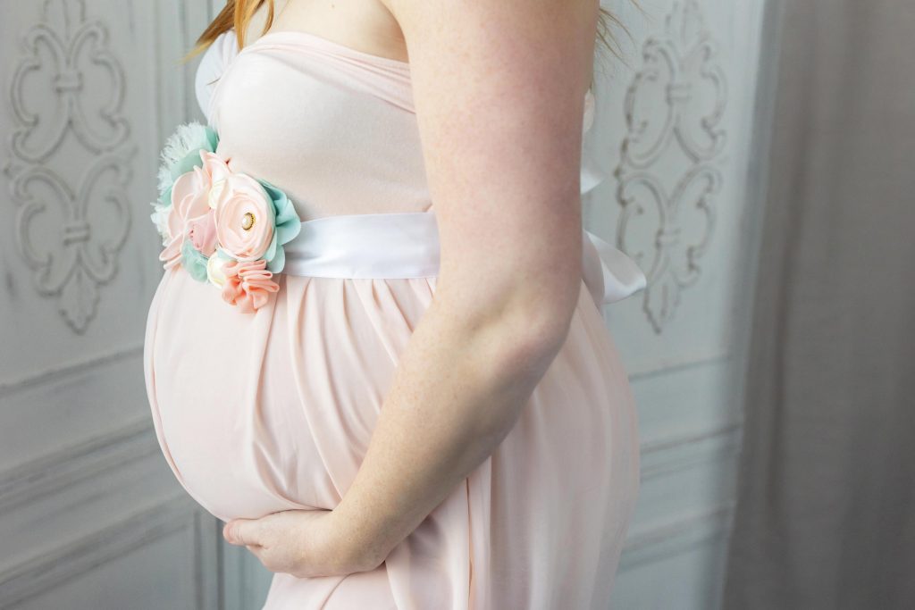What to wear for a maternity photo shoot in Portland, OR. This is a close up belly photo of a pregnant woman wearing a flowy pink dress with a flower belt.