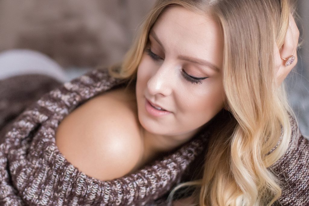 What to wear for a winter photo shoot in Portland.  This is a boudoir image of a woman lying on her tummy, wearing an off the shoulder sweater. Photography by Rayleigh. byRayleigh.com