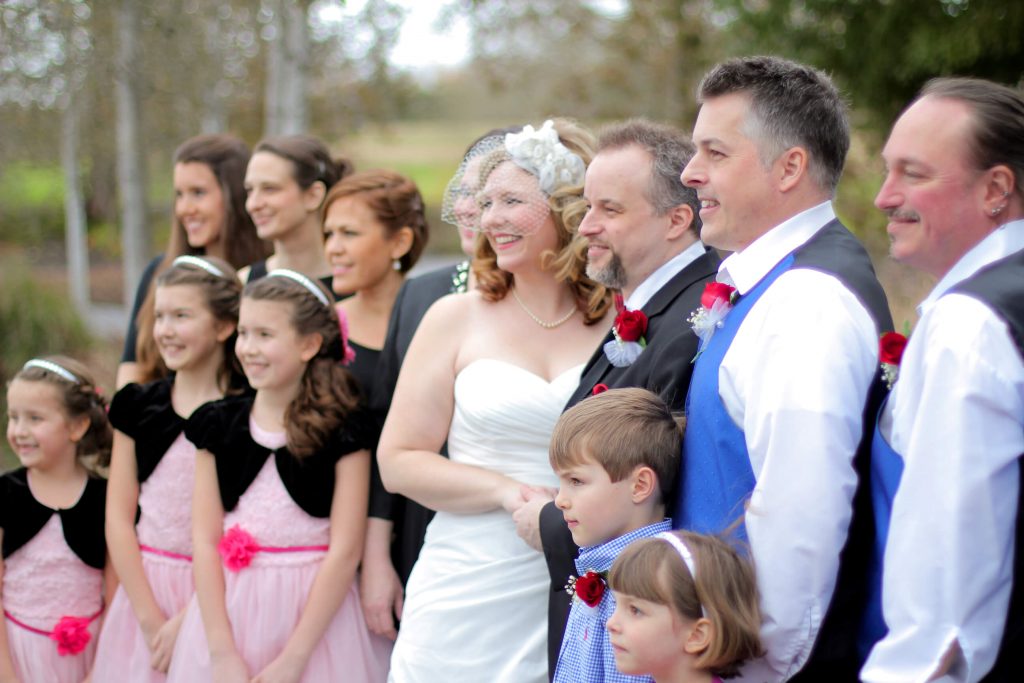 A wedding party smiling for a wedding photo. The posed portrait was taken outdoors behind the Hillsboro public Library near Portland, OR. This was a Valentine's Day wedding.