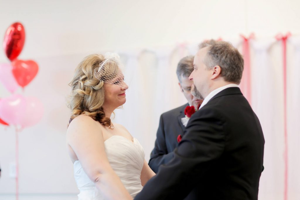 A bride and groom smiling at each other during their Valentine's Day Wedding ceremony. The wedding was held at the library in Hillsboro, OR near Portland, where they also had their couples photo shoot.