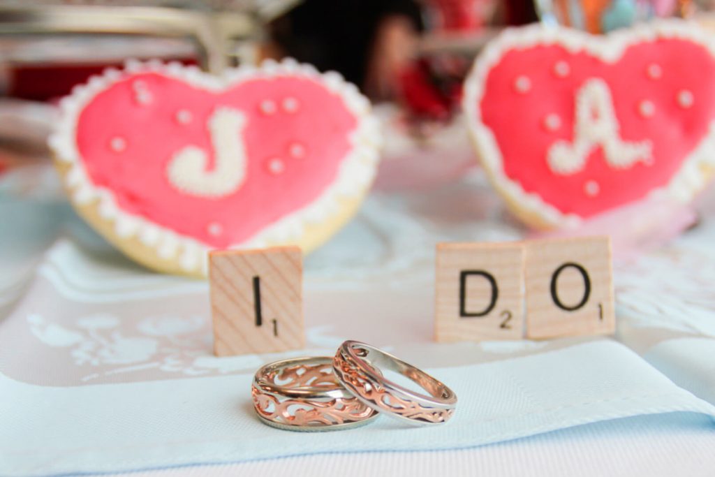 A pair of wedding rings, scrabble pieces, and heart shaped cookies at a Valentine's Day wedding at the library in Hillsboro, OR, near Portland. 