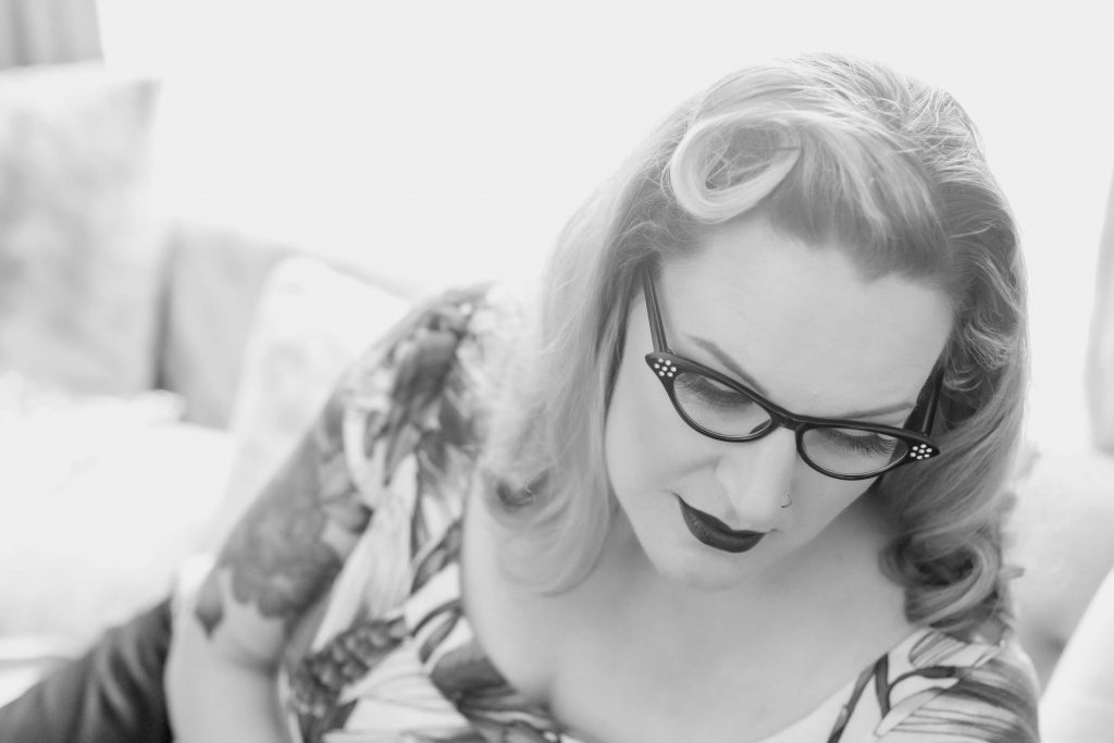 A posed black and white backlit studio image from a pin up photo shoot experience in Portland. Props include vintage inspired eye glasses.