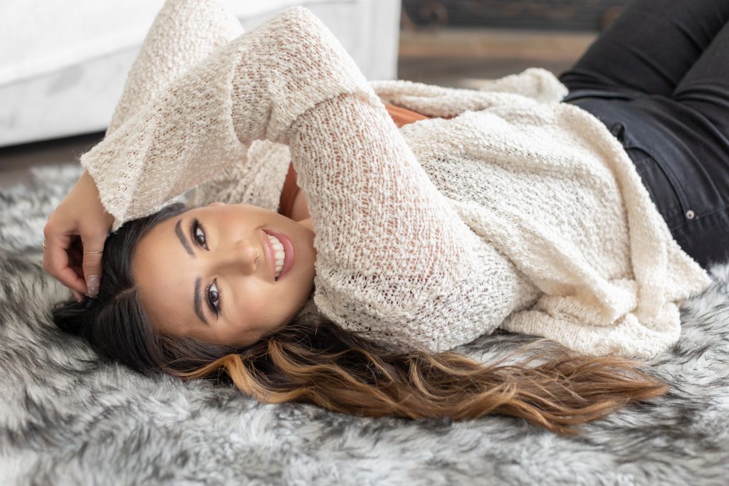 A Fall beauty photo shoot in Portland, Oregon by beauty and boudoir photographer, Photography by Rayleigh. This is a modest boudoir image of a women lying on a rug on the floor, wearing a white sweater and Fall wardrobe.